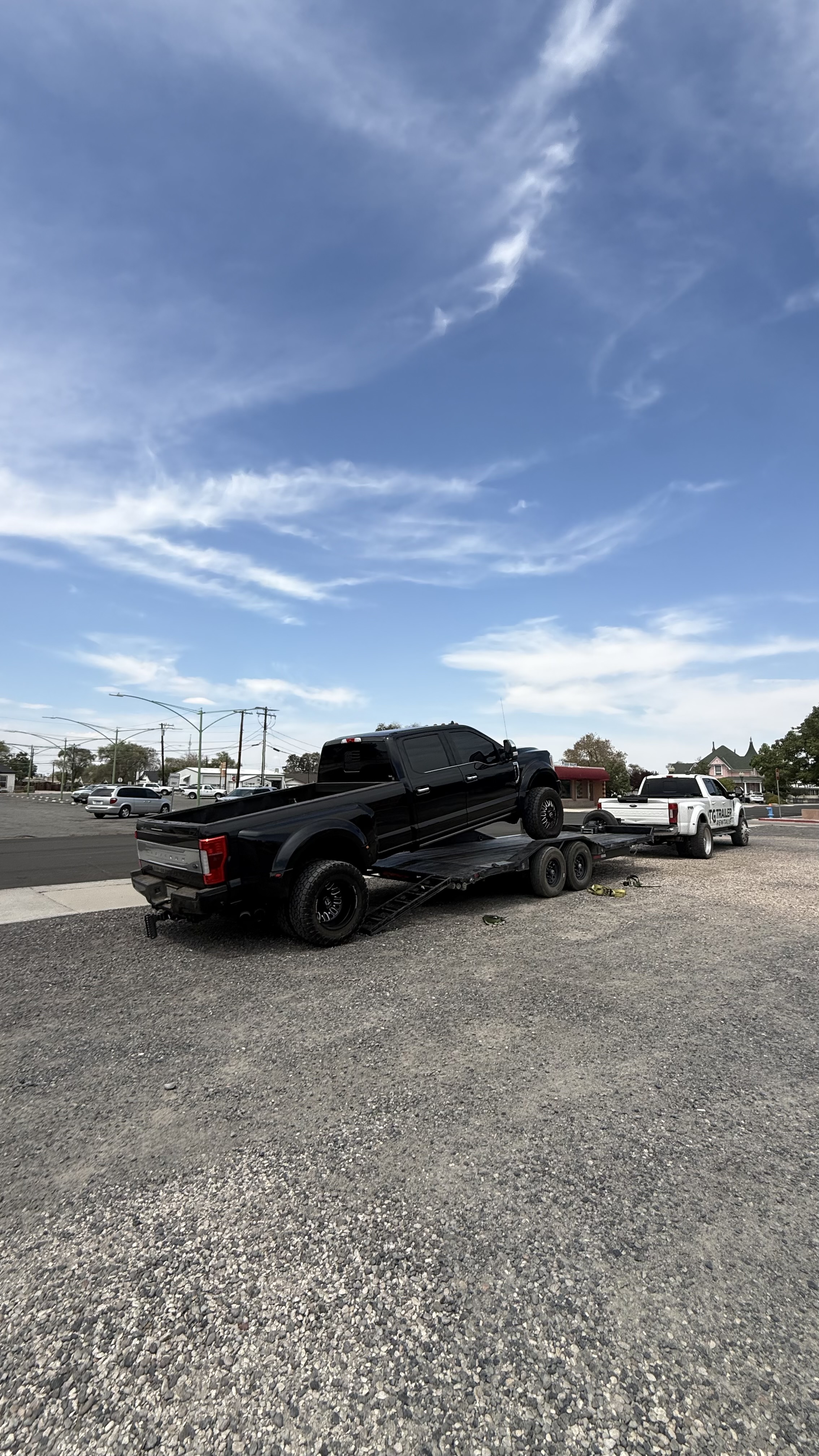 Flatbed trailer attached to a white truck carrying wooden furniture pieces in a parking lot.
