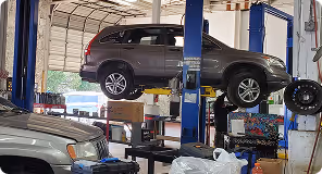 Gray SUV lifted on a car hoist inside a workshop with tools and equipment nearby.