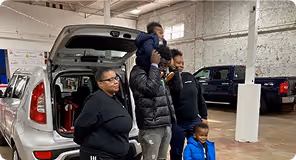 Family of four with two children standing by the open trunk of a silver SUV indoors.