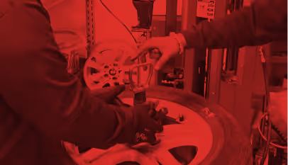Two people working on car tire rims with tools in a workshop.