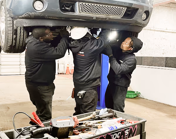Three mechanics working together under a raised vehicle in a spacious garage.