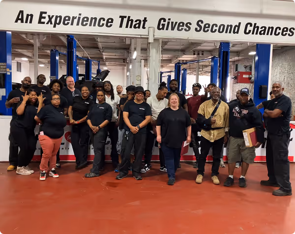 Group of diverse people standing in a workshop under a banner reading 'An Experience That Gives Second Chances'.