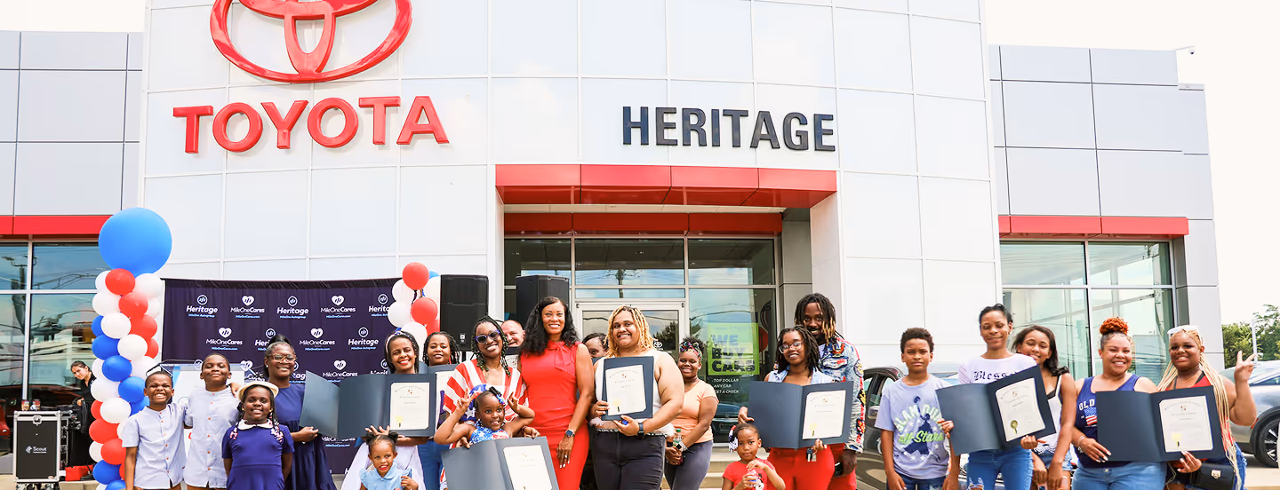 Group of people holding certificates posing outside a Heritage Toyota dealership with balloons.