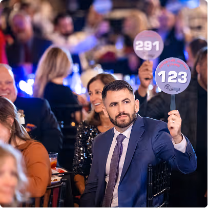 Man in suit raising paddle numbered 123 at an auction event with other attendees.