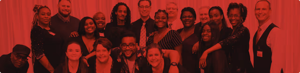 Group of people posing closely together, smiling in front of a curtained backdrop.