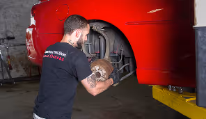 Mechanic working on the exposed wheel hub of a red car in a garage.