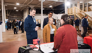 People talking at an indoor event with tables and a staircase in the background.