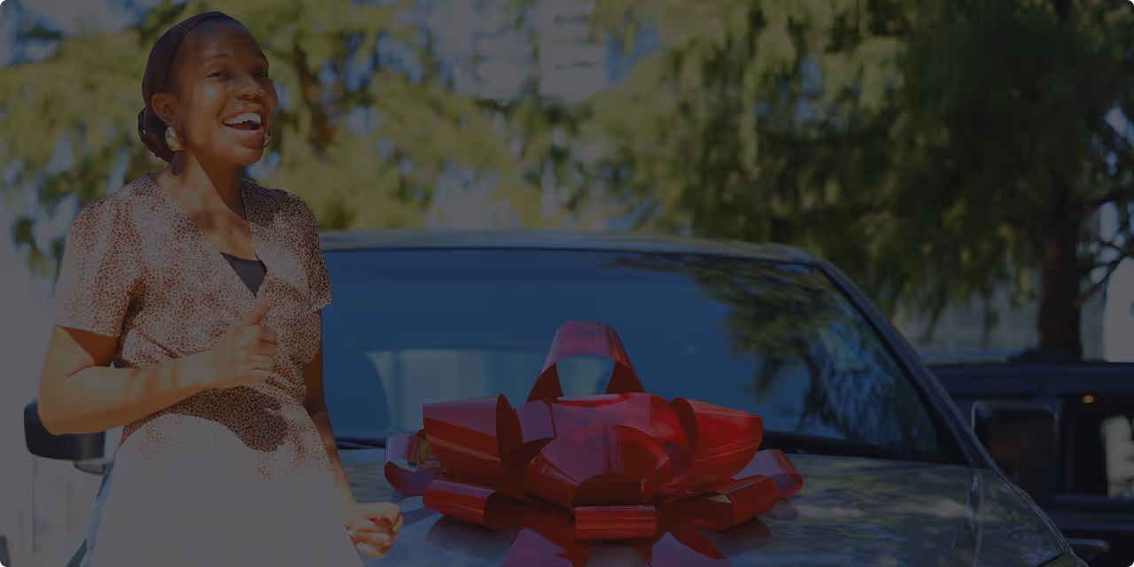 Smiling woman giving thumbs up next to a car hood decorated with a large red bow.