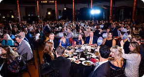 Large group of people seated at round tables during an indoor dinner event.