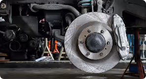 Close-up of a car brake disc and caliper on a vehicle lifted for maintenance.