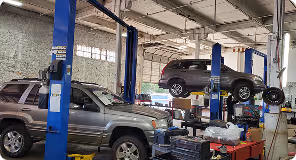 Two SUVs inside a garage, one on a blue lift and the other parked below near tools and tires.