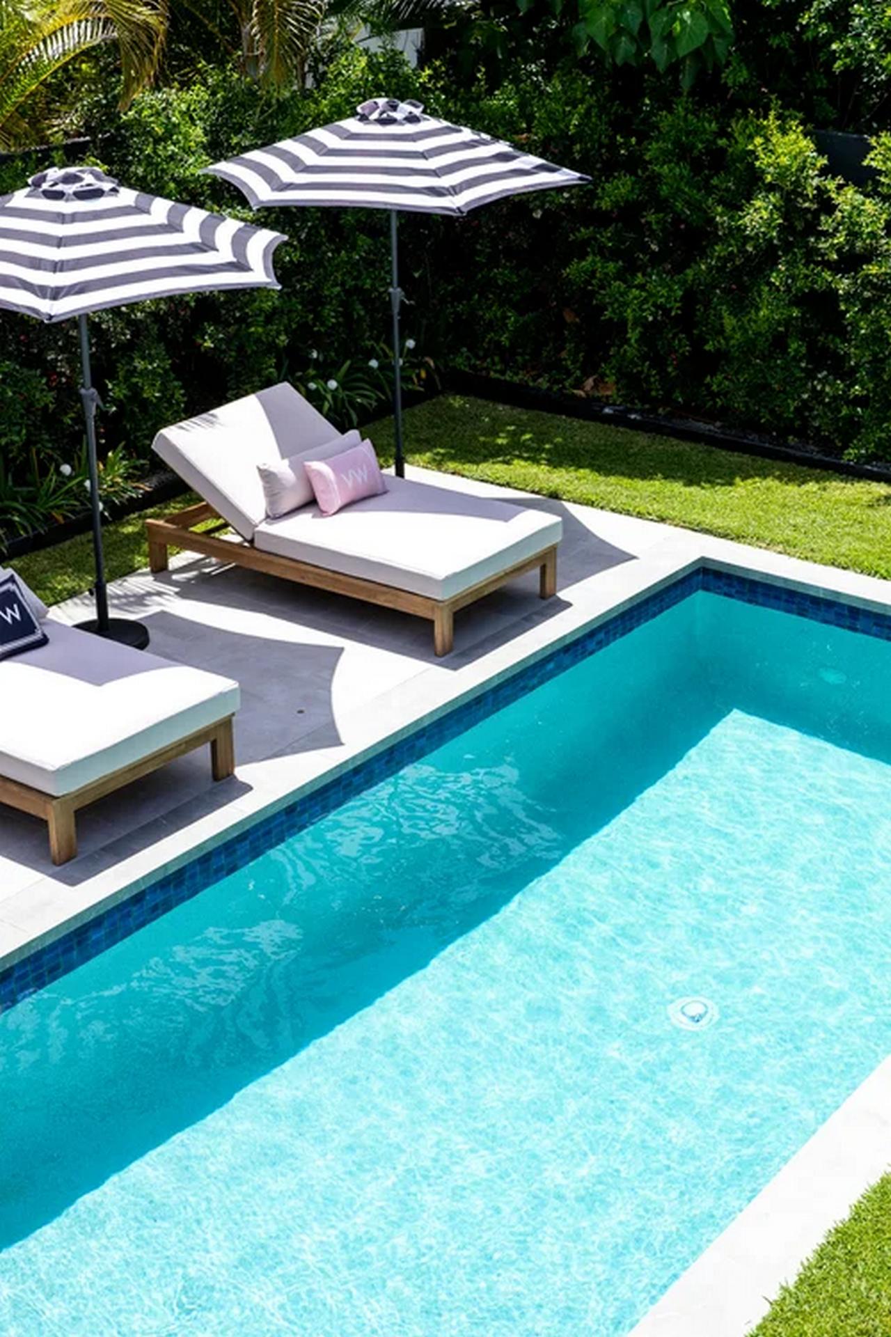 Clear blue swimming pool beside two wooden lounge chairs with white cushions under black and white striped umbrellas.