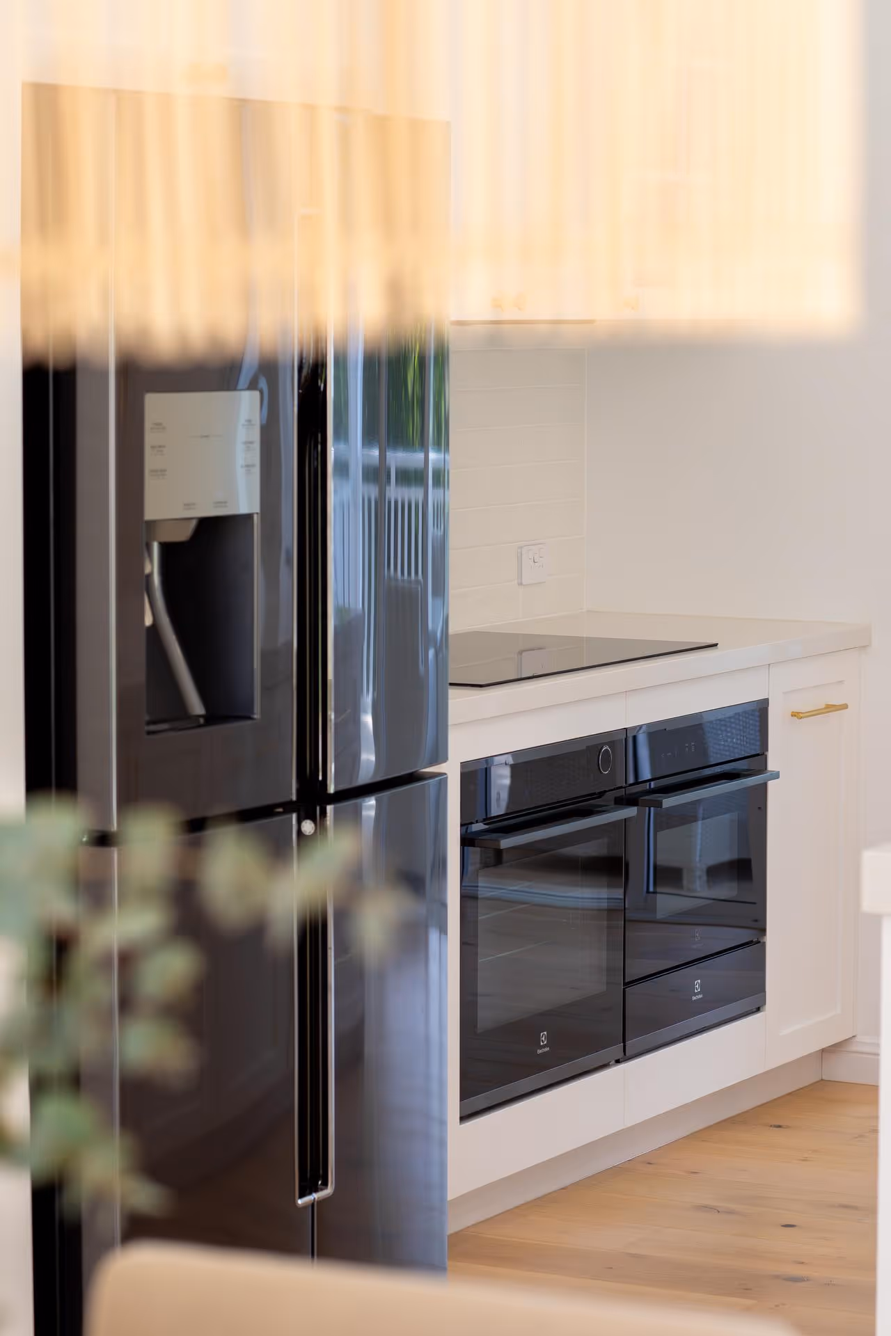 Modern kitchen with black double ovens, black refrigerator with water dispenser, white cabinets, and wooden floor.