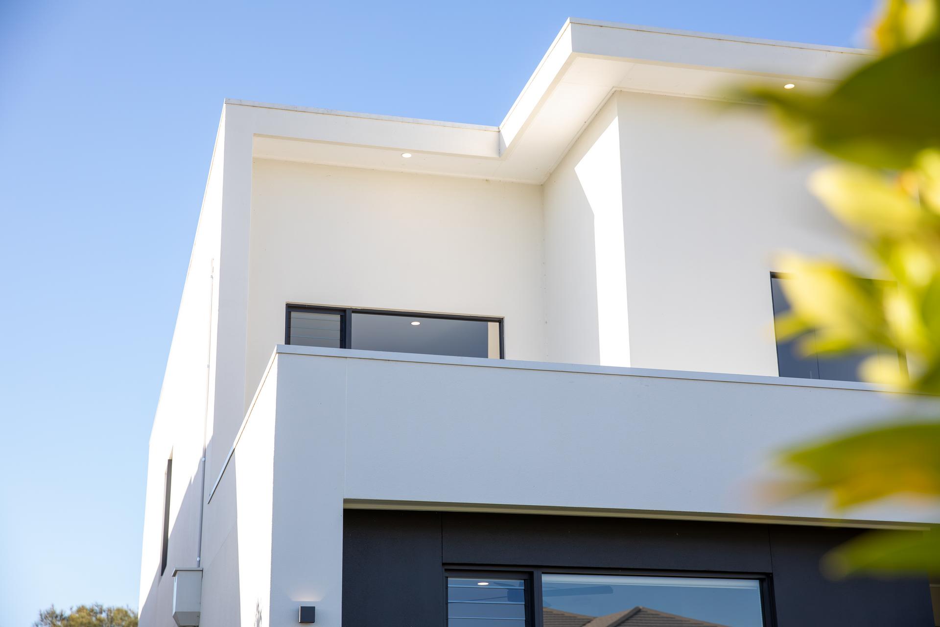 Modern white and black two-story house exterior under clear blue sky with balcony and windows.
