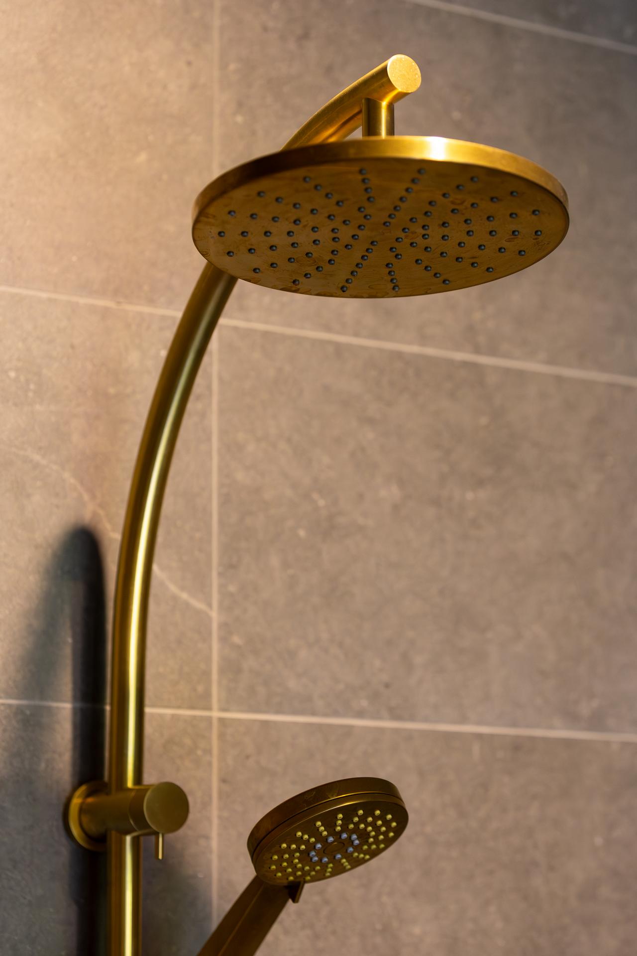 Gold-colored dual shower heads mounted on a tiled bathroom wall.