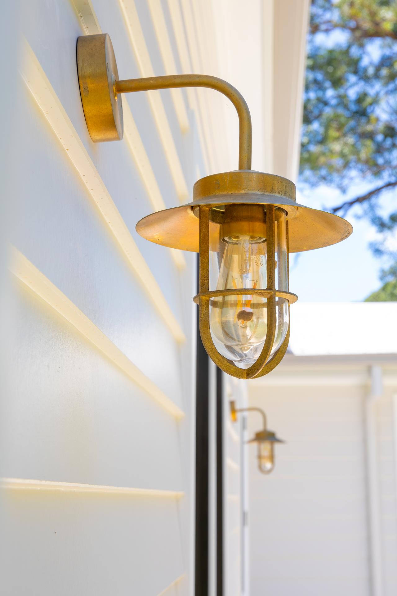 Rustic brass outdoor wall lanterns mounted on a white house exterior under a bright sky.