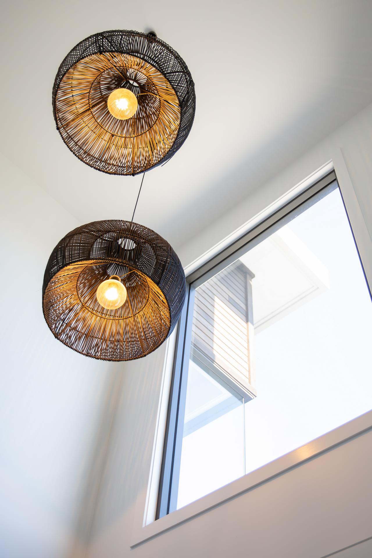 Two woven rattan pendant lights hanging near a large window with bright natural light.