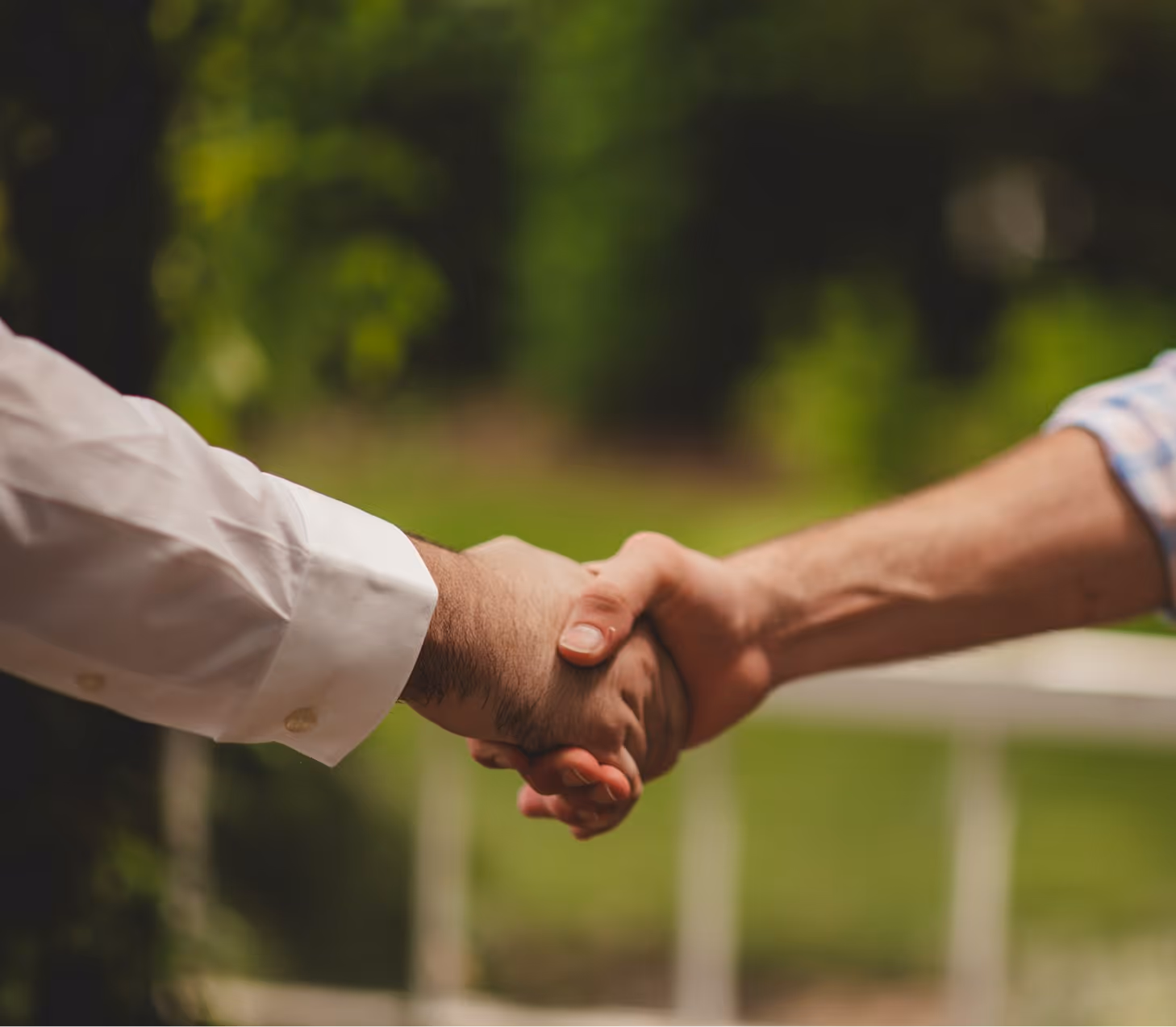 Close-up of two people shaking hands outdoors with blurred green background.