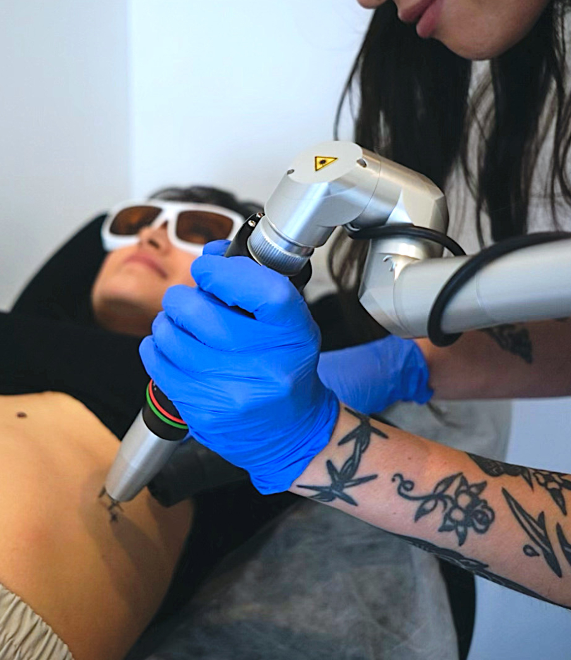 Person wearing blue gloves using a laser device on the stomach of a relaxed client with protective glasses.
