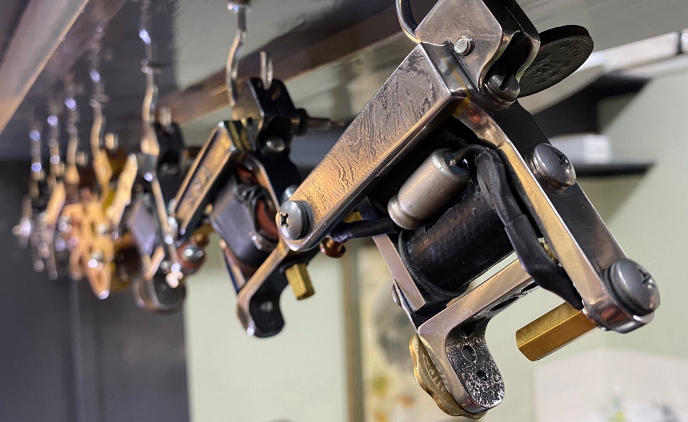 Close-up of several metallic tattoo machines hanging in a row from hooks.