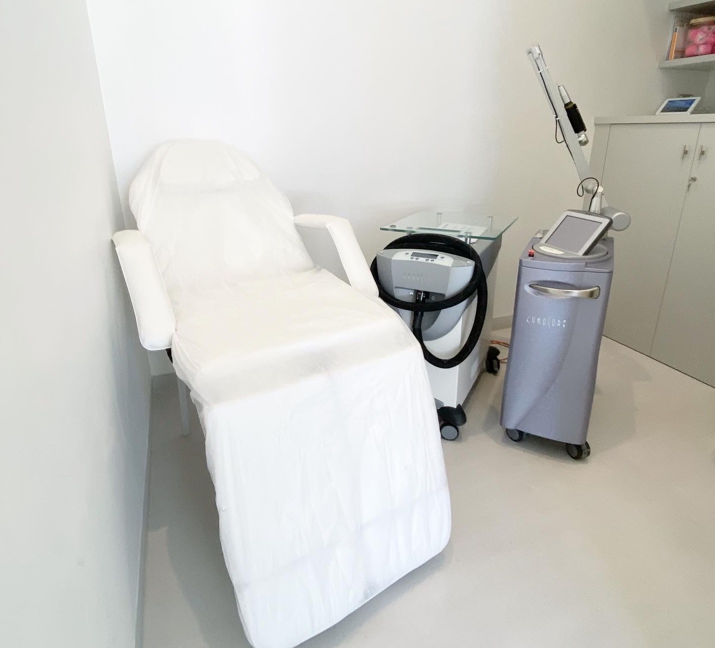 White treatment chair next to a medical laser machine in a clean clinical room.