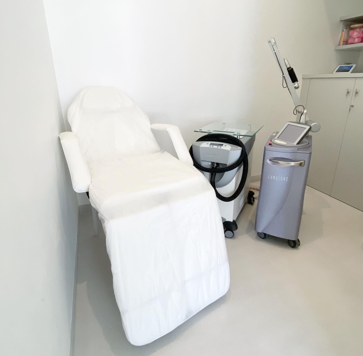 White medical or spa chair next to advanced laser equipment in a clean clinical room.