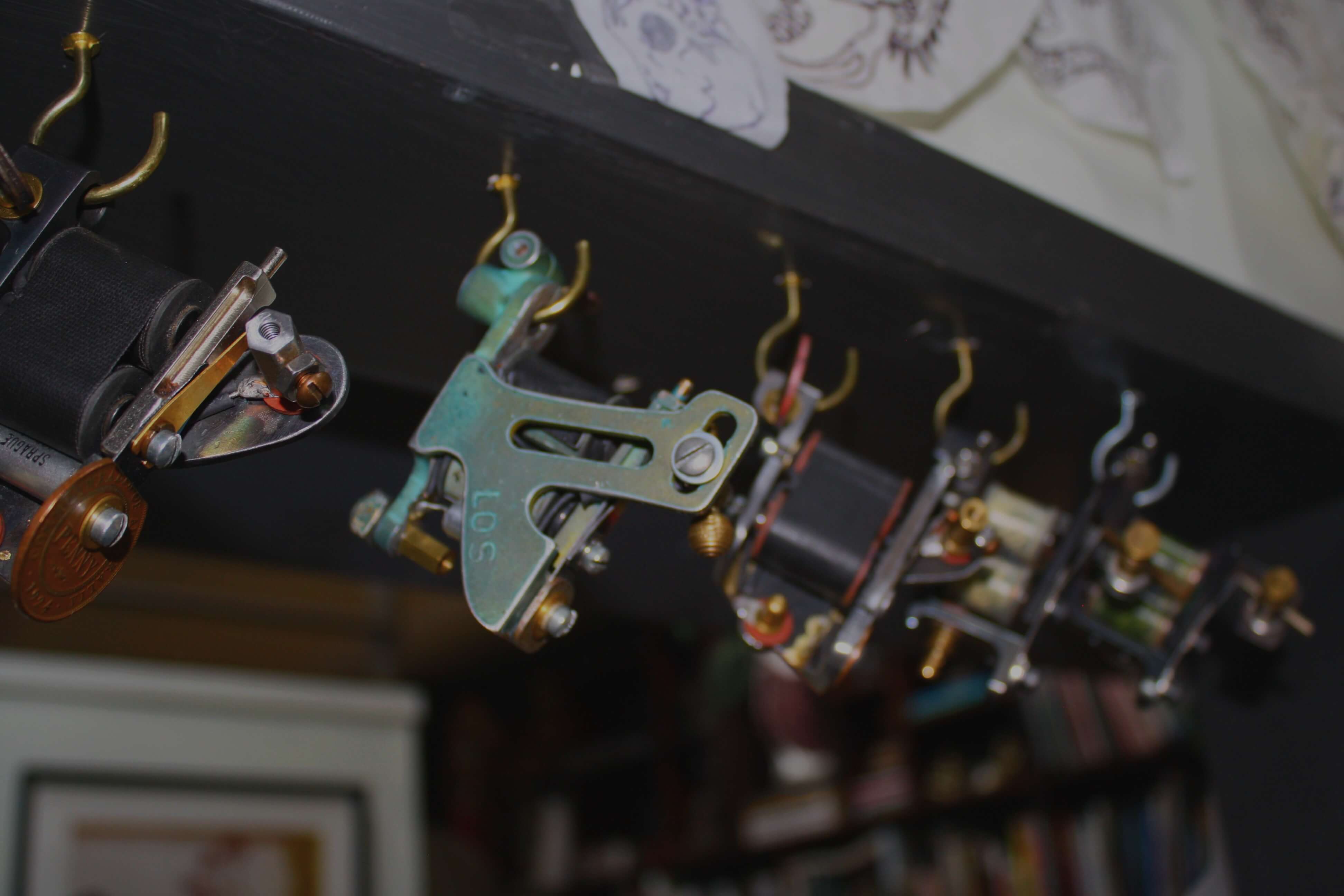 Close-up of vintage tattoo machine coils and frames hanging from hooks indoors.