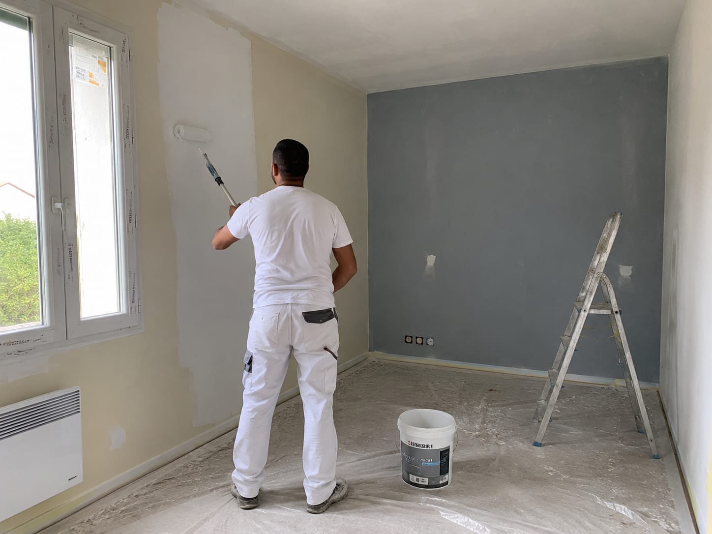Peintre PropNet34 en combinaison blanche rénovant les murs d'un logement dans l'Hérault