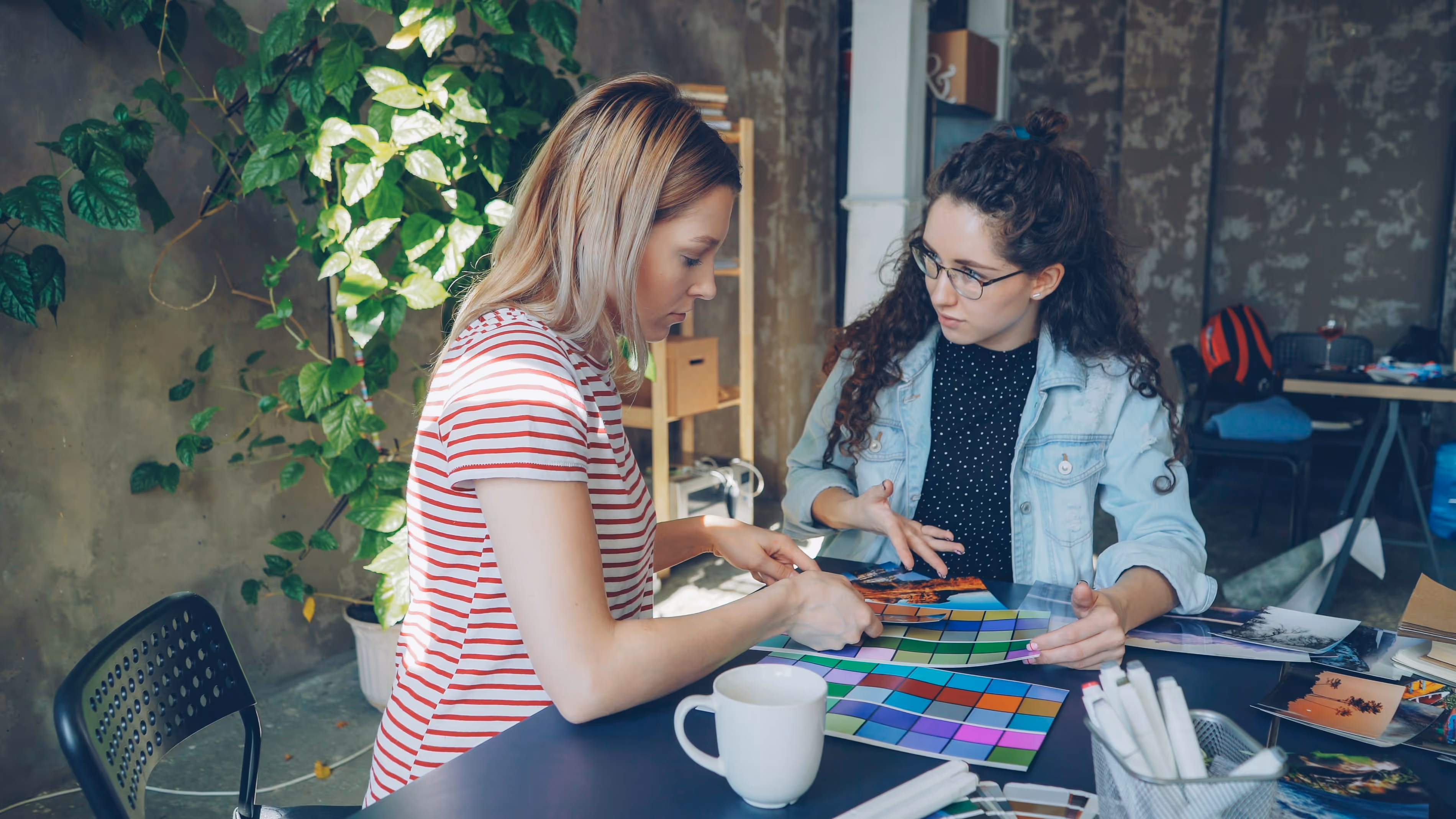 Two women examining color swatches and photos at a table in a casual workspace.