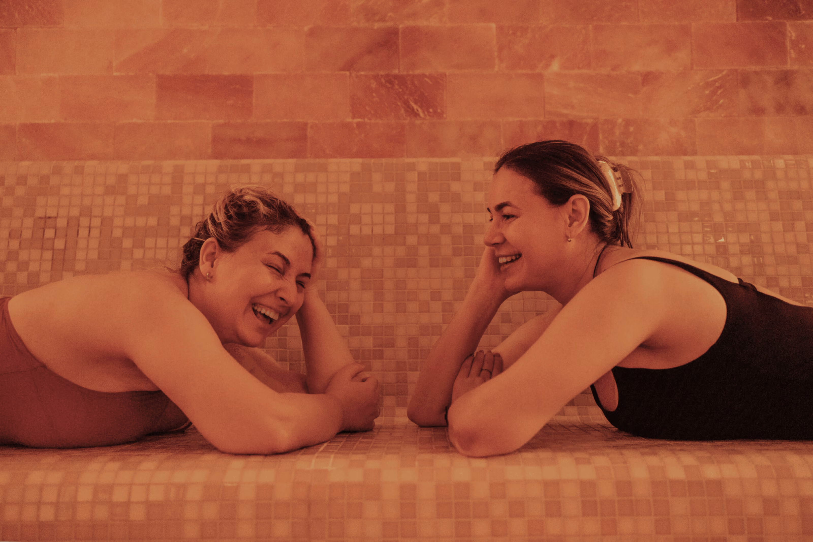 Two Altea members relaxing and laughing in a tiled sauna setting