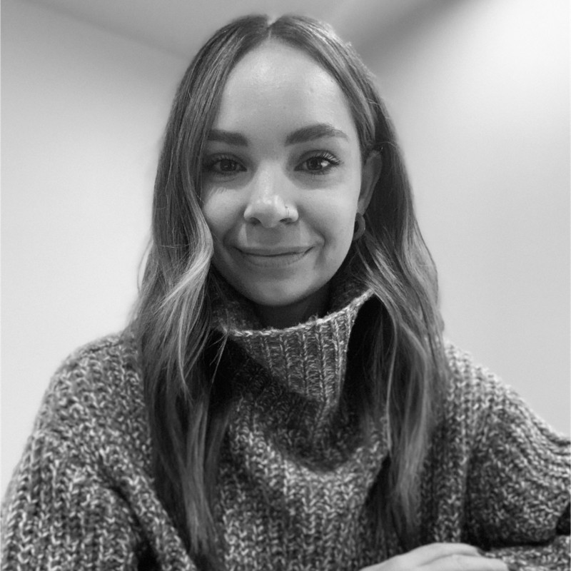 Smiling woman with long hair wearing a knitted turtleneck sweater against a plain background.
