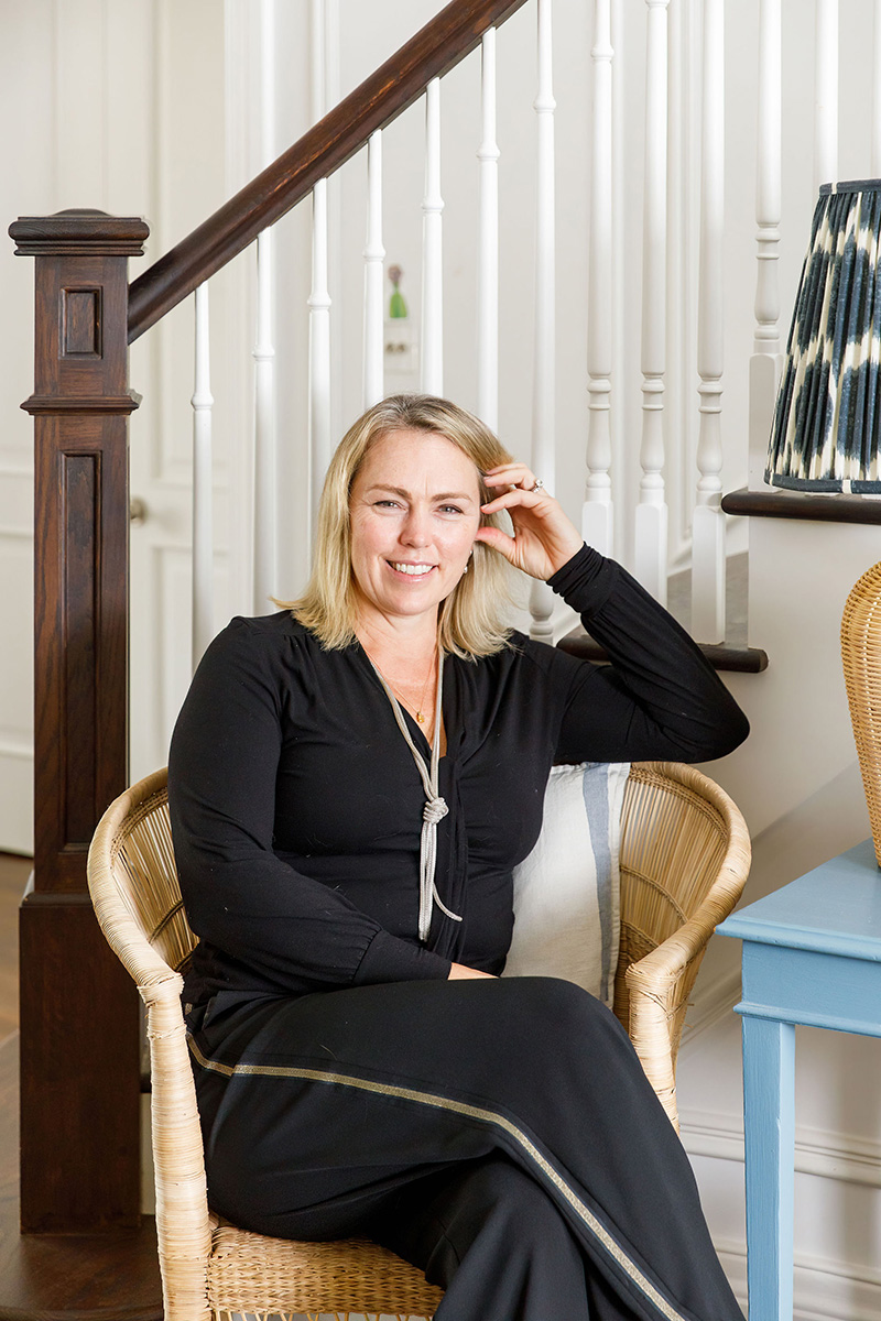 Lorna Smith, interior designer, seated in a wicker chair beside the staircase of a Sussex home she designed