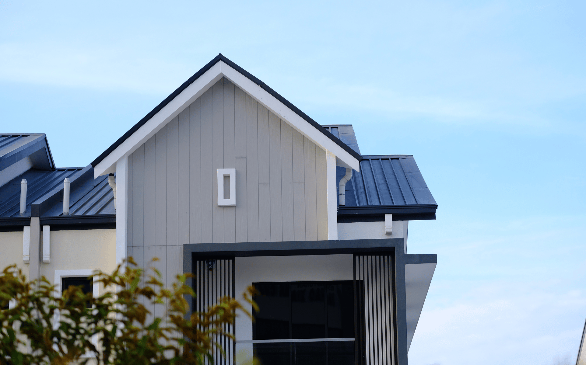 Moderner Hausgiebel mit hell gestrichener Holzfassade, weißen Details und dunklem Dach.