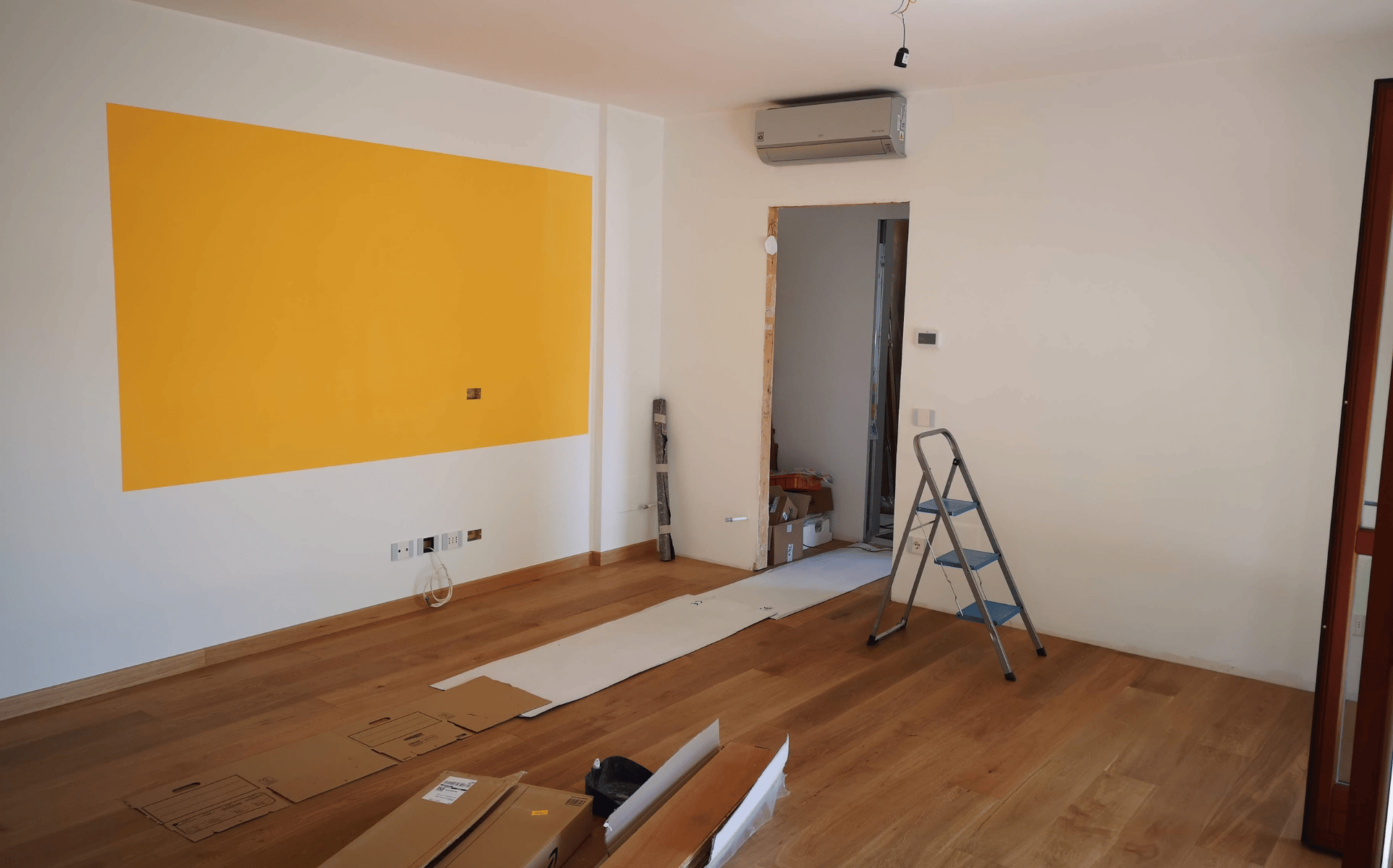 Renovierter Innenraum mit gelber Akzentwand, Leiter und abgedecktem Boden bei Malerarbeiten von Malermeister Jens Meyer in Hamburg.
