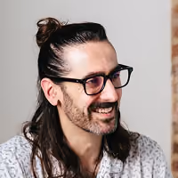 Man with long dark hair tied back, glasses, and a beard smiling while looking right.