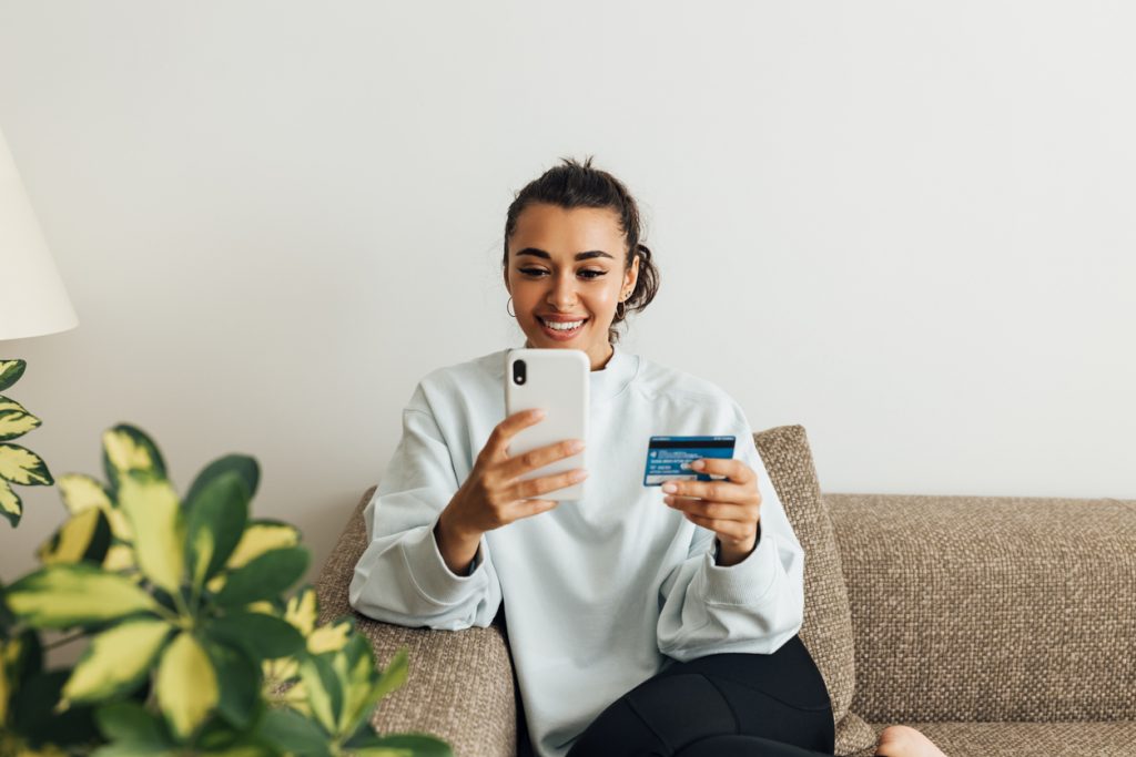 Image Caption: A customer receiving a package from an unseen courier. / A smiling woman making an online purchase using her smartphone and credit card. 