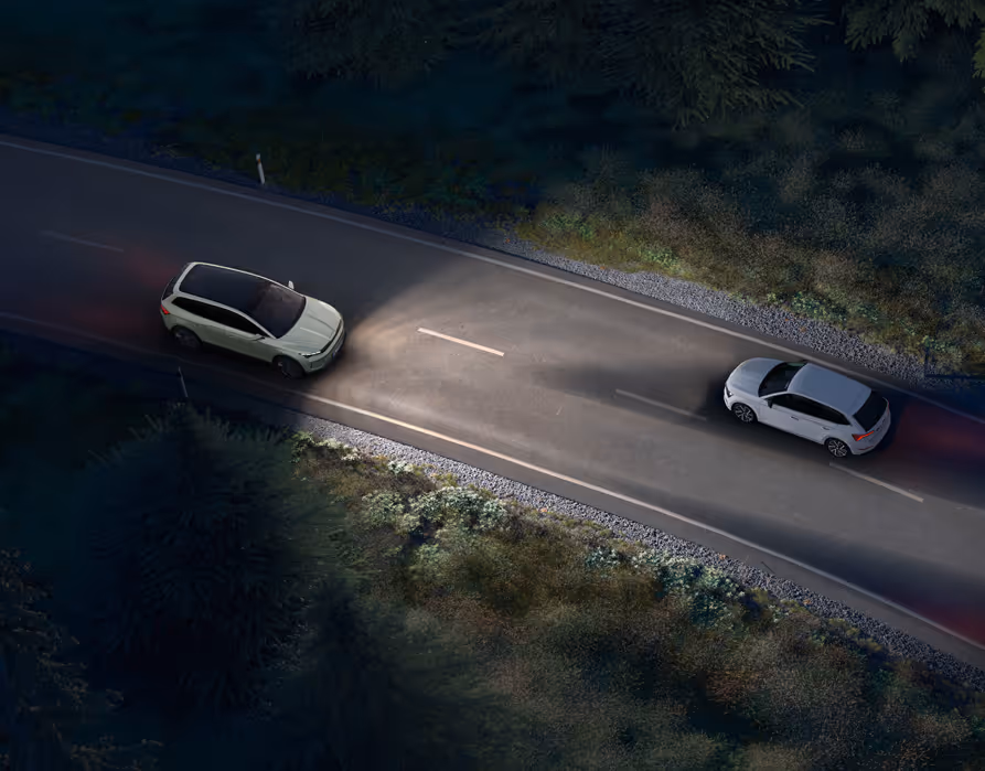 Animation des Dynamischen Fernlichtassistenten: Ein Škoda Epiq fährt nachts auf einer Landstraße und leuchtet die Fahrbahn mit Fernlicht aus. Das System erkennt entgegenkommende und vorausfahrende Fahrzeuge und blendet diese gezielt aus dem Lichtkegel aus, um eine Blendung zu vermeiden.