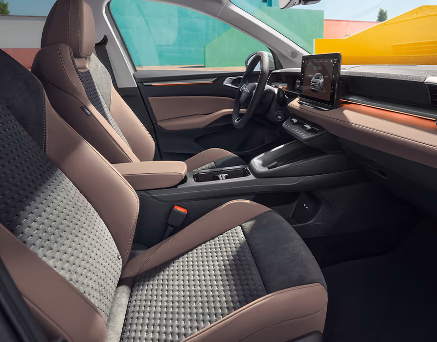Eine seitliche Innenansicht des Škoda Epiq zeigt das Interieur der Design Selection Suite. Die dunklen Sitze mit cognacfarbenen Elementen sowie die Armaturentafel mit passendem Bezug und kupferfarbenen Zierleisten sind zu sehen, während durch die Fenster farbenfrohe, geometrische Gebäudewände sichtbar sind.