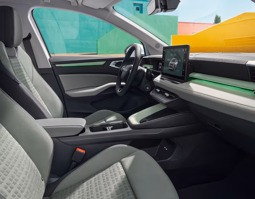 Eine seitliche Innenansicht des Škoda Epiq zeigt das Interieur der Design Selection Loft Mint. Die mintfarbenen Textilsitze mit korrespondierenden Nähten sowie die Armaturentafel mit grauem Techtona und matten Dekorelementen sind zu sehen, während durch die Fenster farbenfrohe, geometrische Gebäudewände sichtbar sind.