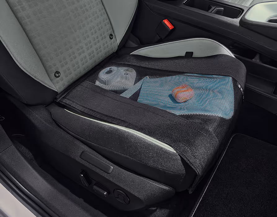 Blick auf den Beifahrersitz im Škoda Epiq, auf dessen Sitzfläche ein praktisches schwarzes Ablagenetz befestigt ist. Unter dem Netz sind verschiedene Gegenstände wie ein eine blaue Mappe sicher und griffbereit verstaut. An der Seite des zweifarbigen Sitzes befinden sich die Bedienelemente für die elektrische Sitzverstellung.