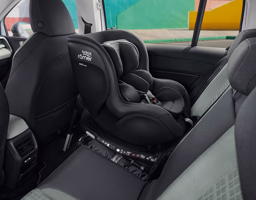 Blick in den Fond des Škoda Epiq auf die hintere Sitzreihe, wo ein schwarzer Kindersitz der Marke Britax Römer montiert ist. Zum Schutz der Sitzpolsterung befindet sich unter dem Reboarder-Sitz eine passgenaue dunkle Schutzmatte. Im linken Bildbereich sind die Rückseiten der dunklen Vordersitze sowie die Mittelkonsole mit integrierten Lüftungsschlitzen zu erkennen.
