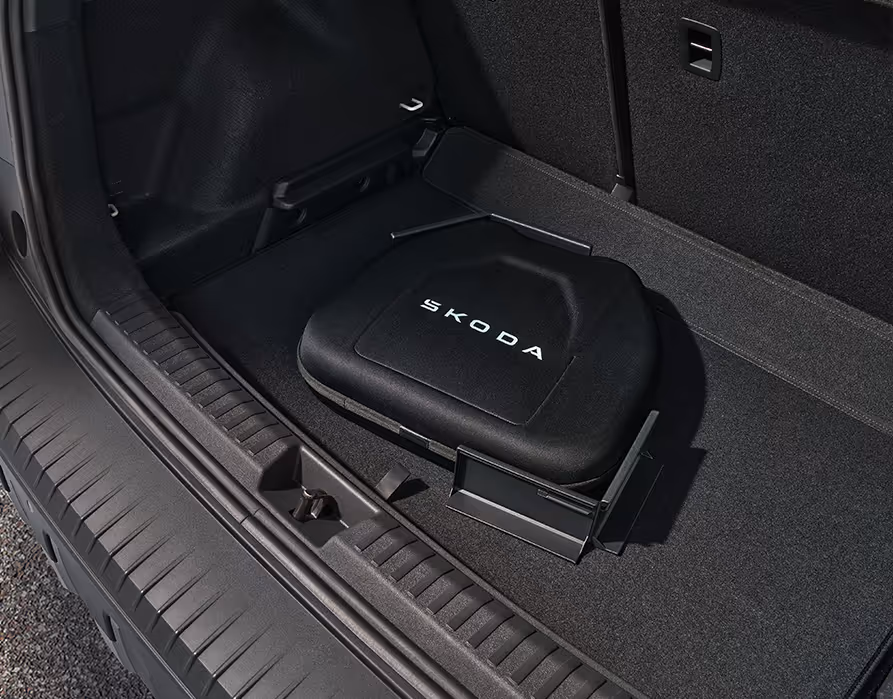 Detailaufnahme des Kofferraumbodens im Škoda Epiq mit einer darauf platzierten schwarzen Ladekabeltasche. Die Tasche trägt einen weißen Škoda-Schriftzug und wird durch ein winkelförmiges Cargoelemente auf der Bodenmatte gesichert. So wird ein Verrutschen des Ladezubehörs während der Fahrt effektiv verhindert.