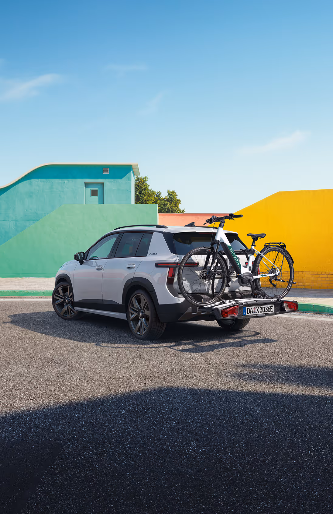 Heckansicht eines Škoda Elroq mit einem Fahrradträger auf der Anhängerkupplung vor grünem Studiohintergrund. Auf dem Träger sind zwei Fahrräder mit Škoda Schriftzug auf dem Rahmen montiert.