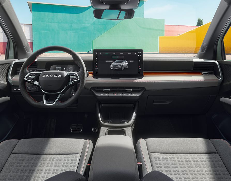 Eine weite Innenansicht zeigt das Cockpit des Škoda Epiq als Sondermodell "First Edition", dessen Interieur auf der Design Selection Loft Grau basiert. Ergänzend zu den grauen Textilsitzen und dem zentralen Infotainment-Display setzen spezifische orangefarbene Akzente an der Armaturentafel farbige Kontraste. Darüber hinaus unterstreichen rote Ziernähte sowie auffällige rote Sicherheitsgurte den besonderen Charakter des Innenraums.