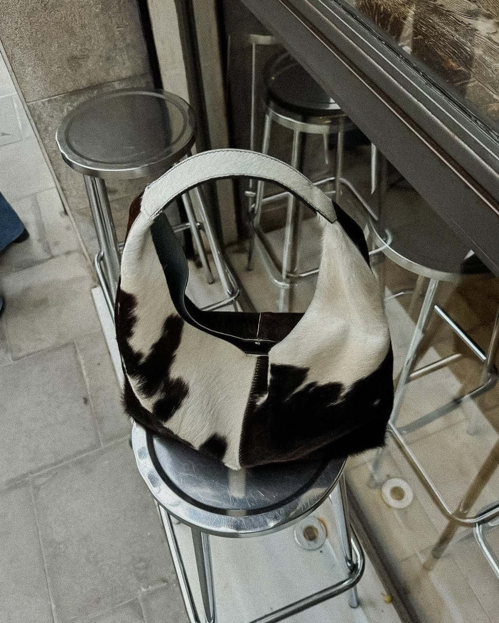 Edgy Fashion-Statement mit einer gemusterten Fellhandtasche auf einem Metallhocker als Symbol für individuelle Markenidentität von UNBOTHERED®.