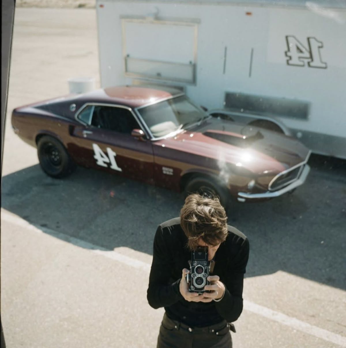 Fotograf mit Vintage-Kamera inszeniert eine Content-Strategie vor einem klassischen Ford Mustang Rennwagen für das UNBOTHERED® Studio.