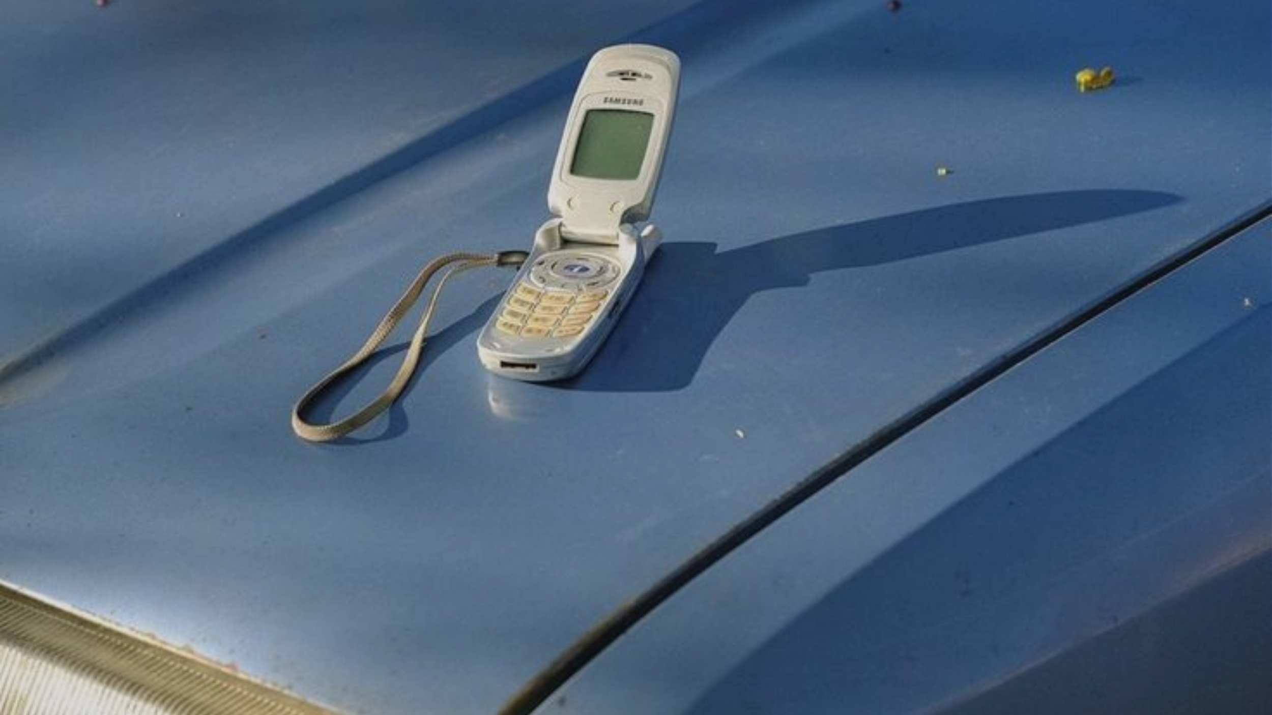 Klassisches, silbernes Klapphandy der 2000er Jahre geöffnet auf einer hellblauen Automotorhaube für die Kontaktseite des Branding-Studios UNBOTHERED®.