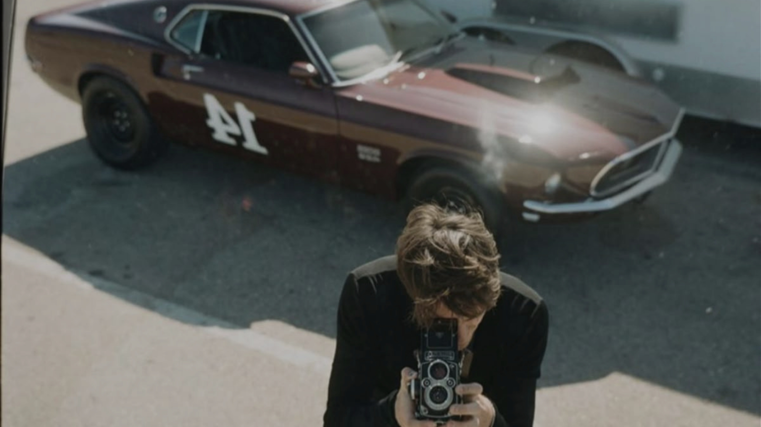 Fotograf mit Vintage-Kamera inszeniert eine Content-Strategie vor einem klassischen Ford Mustang Rennwagen für das UNBOTHERED® Studio.