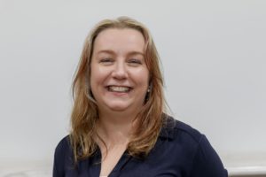 Smiling woman with shoulder-length brown hair wearing dark blue top against white background