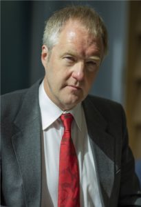 Professional headshot of middle-aged man in dark suit and red tie